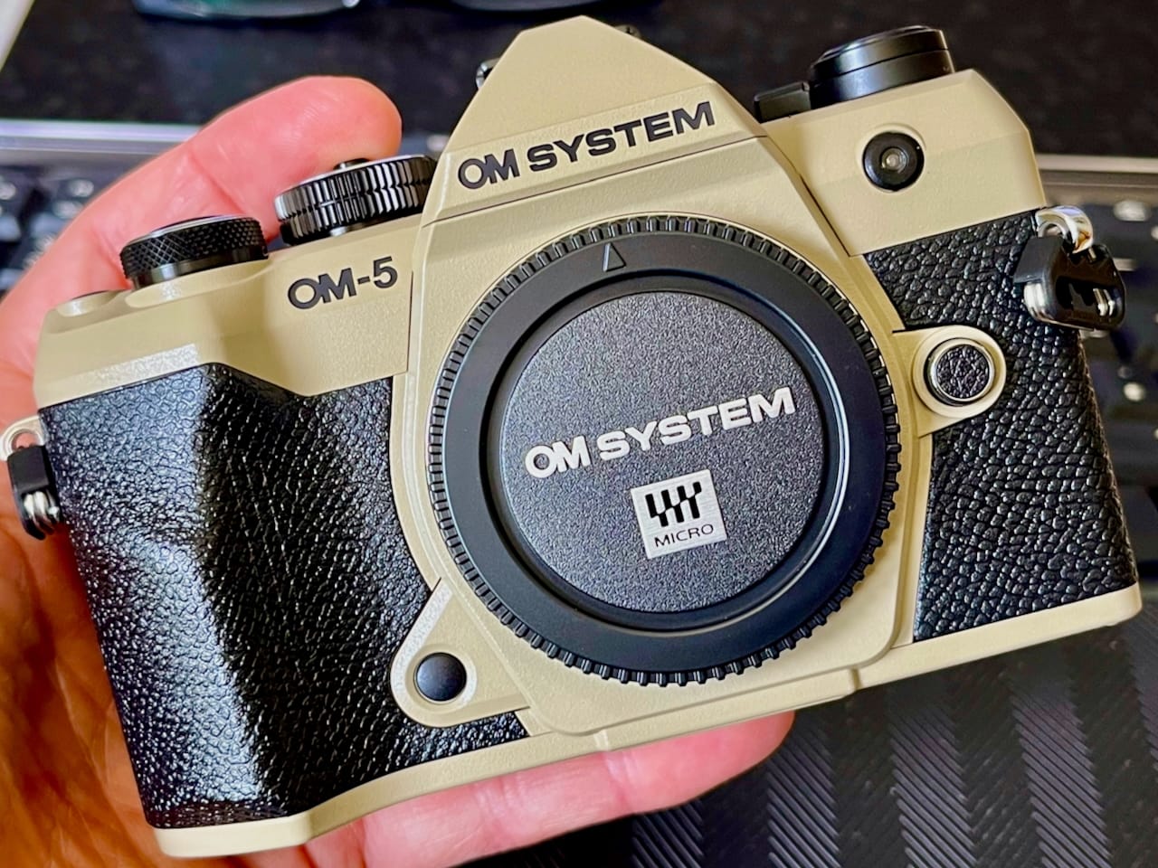 Front view of an OM-5 in sand beige. It's being held by a hand.